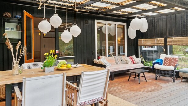 A modern outdoor dining area with a wooden table, chairs, and hanging white lanterns.