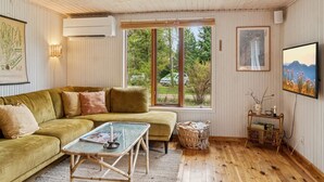 A cozy living room with a green sofa, a small table, and a window with a view of trees.