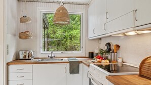 A kitchen with white cabinets, a wooden countertop, a hanging wicker light, and a window with a view of greenery.