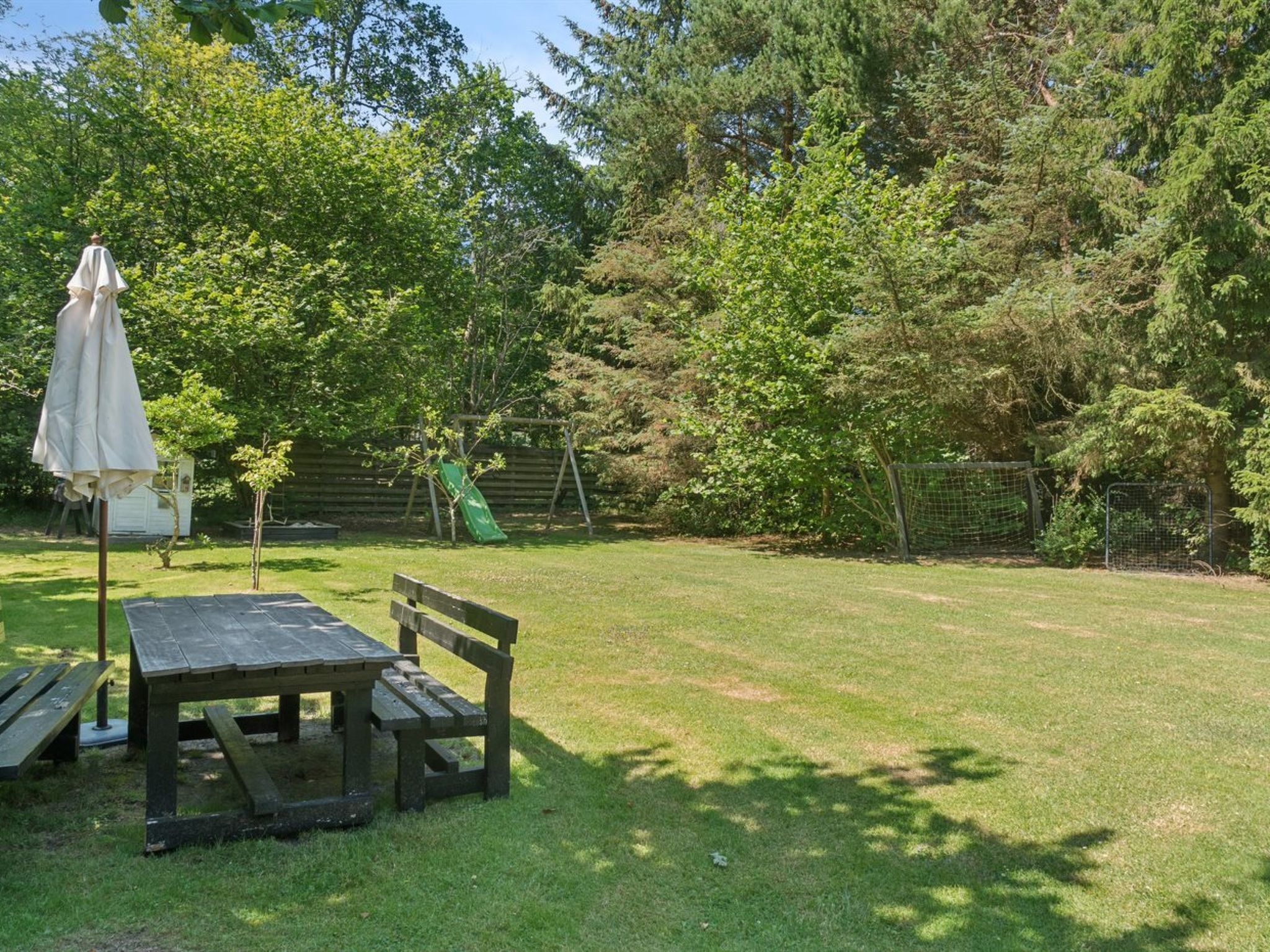 A picnic table and bench in a grassy backyard with a wooden fence and trees.