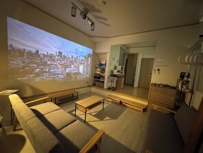 Ein modernes Wohnzimmer mit großem Bildschirm, der eine Stadtansicht zeigt, einer Couch, einem Couchtisch und einer hölzernen Bank.