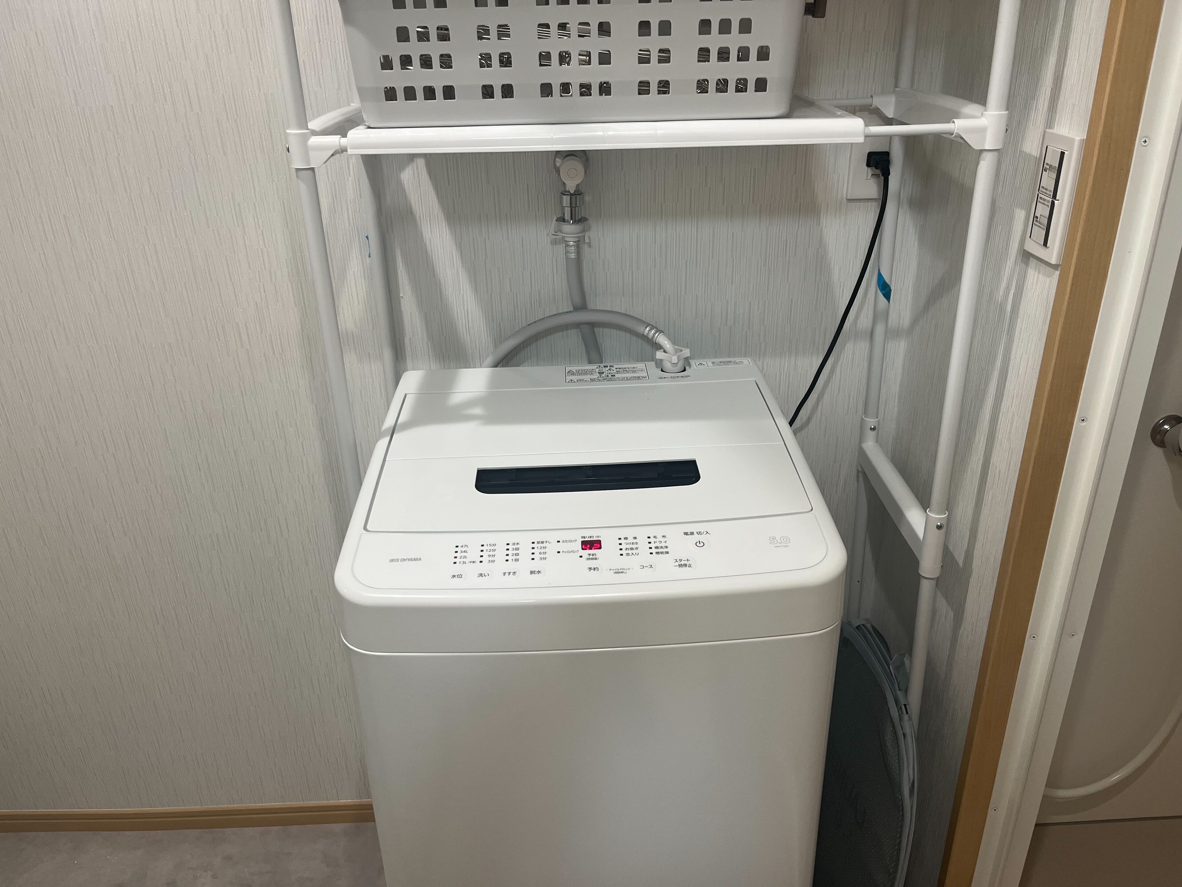 A compact, white, front-loading washing machine with a control panel, a power cord, and a water hose.