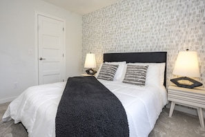 Quarto com cama, duas mesas de cabeceira com abajures, uma porta e papel de parede estampado.