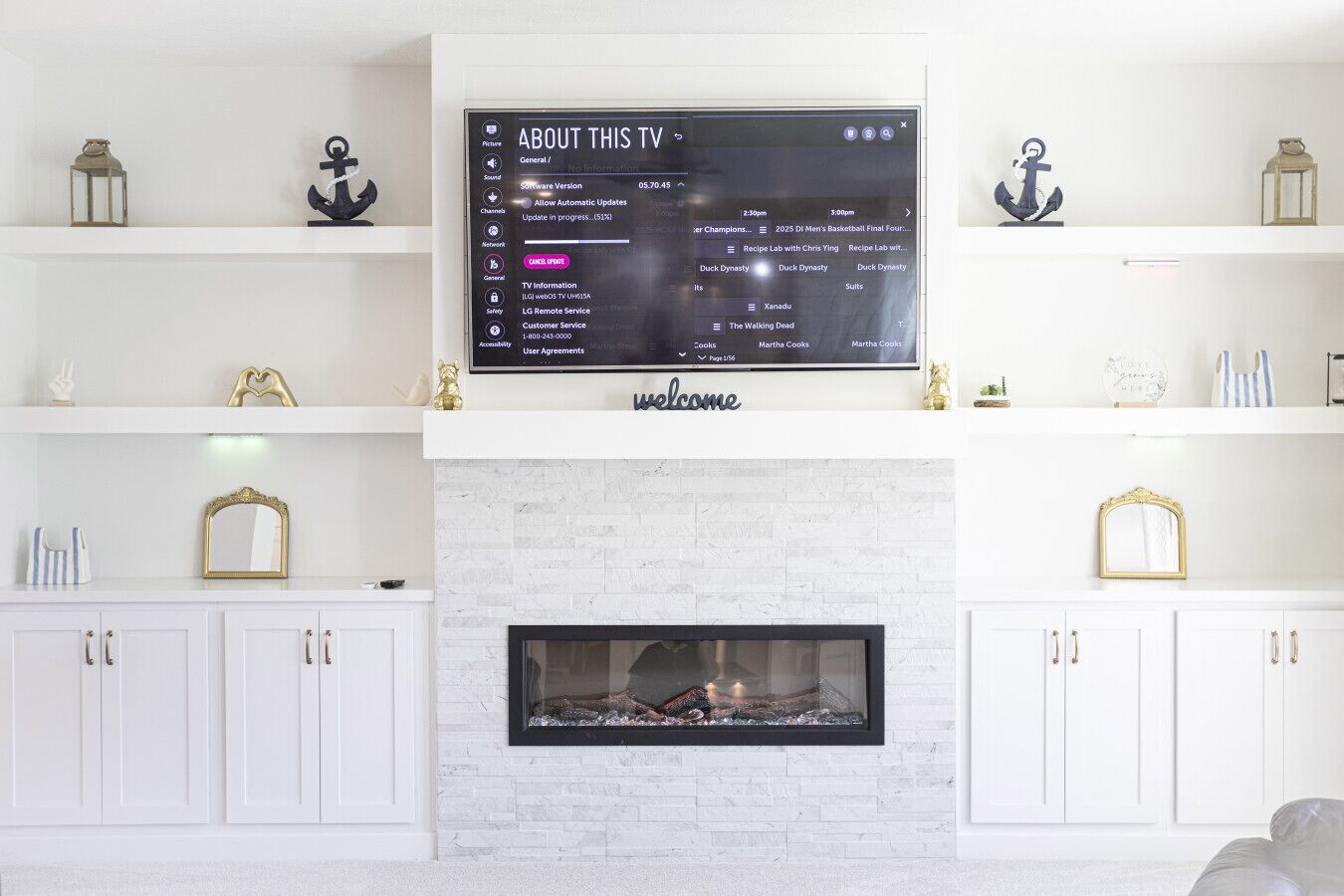 Una sala moderna con un televisor de pantalla plana sobre la chimenea, armarios blancos y objetos decorativos en estantes.