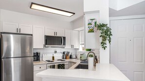 Une cuisine moderne avec des meubles blancs, un réfrigérateur en acier inoxydable, un four à micro-ondes et une cuisinière à gaz.