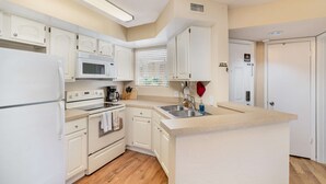 Una cocina pequeña con gabinetes blancos, un microondas, estufa y lavaplatos.