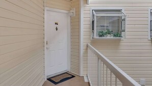 Una puerta blanca con un buzón, una ventana pequeña con persianas, y una barandilla blanca.