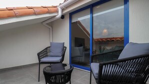 A balcony with two wicker chairs and a small table, a sliding glass door, and a tiled floor.