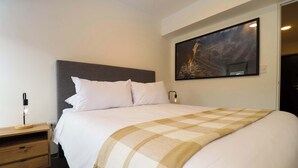 A neatly made bed with a checkered throw blanket, a bedside table with a lamp, and a wall-mounted painting.