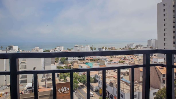 A view from a balcony overlooking a coastal cityscape with buildings, a road, and a beach in the distance.