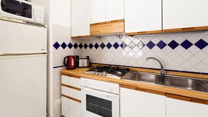 Cocina con armarios blancos, microondas, hervidor, tostadora, estufa y lavabo.