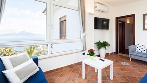 En stue med et stort vindue, et fladskærms-tv, en sofa, et lille bord og en potteplante.
