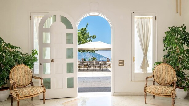 A hotel lobby with a view of an outdoor terrace, two wicker chairs, and potted plants. - Villa Lamaro with sea view - My Rental Homes (Sant'agnello)