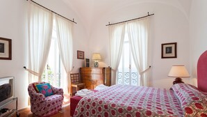 A hotel room with two beds, a wooden dresser, a chair, a TV, and a balcony with a railing.