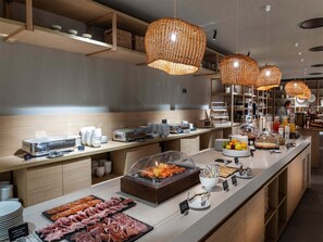 Zona de buffet amb diversos plats, incloent carns i fruites, i llums penjants de vimet.