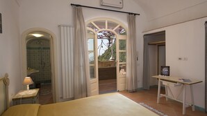 Ein Schlafzimmer mit Bett, Schreibtisch und Blick auf einen Garten durch eine geöffnete Tür.