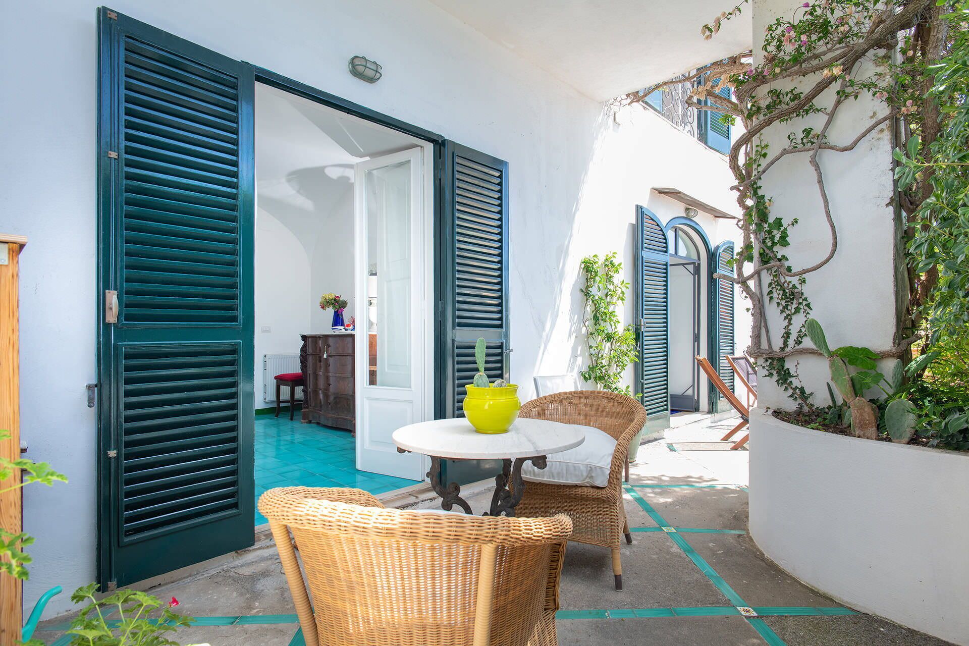 Un pequeño patio exterior con sillas de mimbre, una mesa redonda y una maceta amarilla.