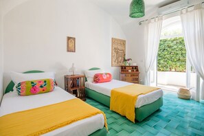 Une chambre avec deux lits, une table de chevet en bois, un mur vert et une fenêtre avec des rideaux.