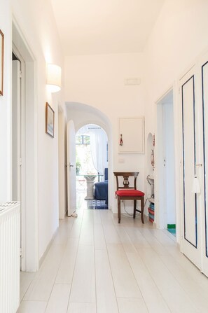 Un couloir aux murs blancs, une chaise en bois avec un coussin rouge et une porte sur la droite.