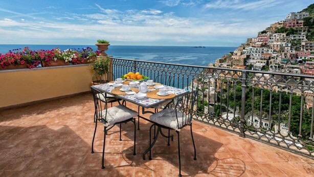 Eine Terrasse mit Tisch für zwei Personen, mit Blick auf eine Küstenstadt und das Meer.