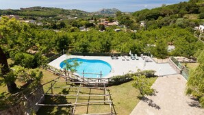 A swimming pool with a wooden deck and lounge chairs, surrounded by greenery and a mountainous backdrop. - Villa Castore with private pool - My Rental Homes (Massa Lubrense)