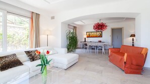 A modern living room with a white sofa, a red armchair, and a dining area with a table and chairs. - Villa Castore with private pool - My Rental Homes (Massa Lubrense)