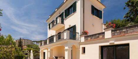 Un bâtiment à deux étages doté d’un balcon, d’un patio couvert aménagé avec du mobilier d’extérieur et d’une grande porte-fenêtre coulissante.