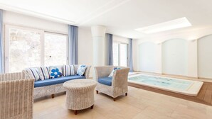 A modern indoor pool area with a sofa and two chairs, a small round table, and a hot tub. - Villa Castore with private pool - My Rental Homes (Massa Lubrense)