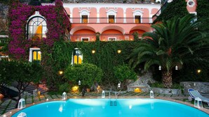 A pool area with a clear blue pool, surrounded by a stone wall, and a building with arched windows and balconies. - Villa Elyseum with swimming pool - My Rental homes (Positano)