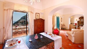 A room with a dining table set for two, a chandelier, and a view of a coastal area. - Villa Elyseum with swimming pool - My Rental homes (Positano)