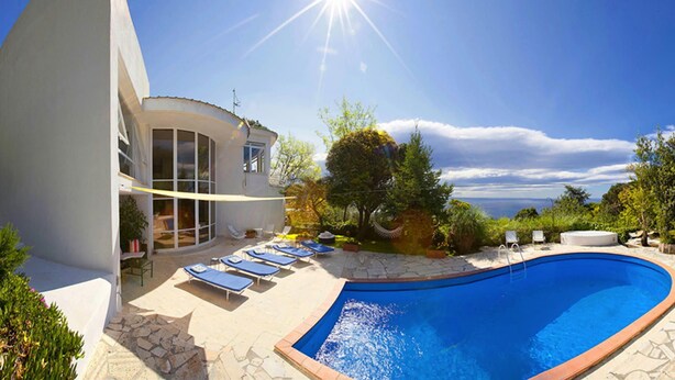 Una casa moderna con piscina, tumbonas y vistas al mar.