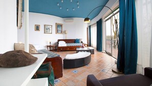 Una habitación moderna con cama, sofá, mesa de comedor y un amplio ventanal con cortinas.