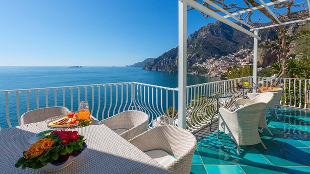 A terrace with wicker furniture, a table with drinks and flowers, and a view of the sea and mountains. - Villa Magnolia with hot tub - My Rental homes (Positano)