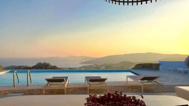 A poolside area with lounge chairs, a table with a bowl and a book, and a view of the sea and distant hills. - My Rental Homes - Villa Pirgi with swimming pool and panoramic sea views. (Paraga)