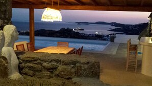 A covered outdoor seating area with a table and chairs, overlooking a body of water with boats and distant land. - My Rental Homes - Villa Pirgi with swimming pool and panoramic sea views. (Paraga)
