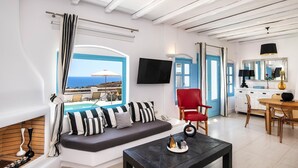 A modern living room with a sofa, a red chair, a coffee table, and a TV. There is a view of the sea through a window. - My Rental Homes - Villa Tramountana with pool and large outdoor spaces with BBQ (Fira)