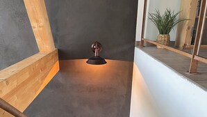 Un escalier avec une rampe métallique, un luminaire fixé au mur et une plante posée sur une étagère.