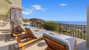 Un balcon avec des fauteuils de jardin, un pilier en pierre et une vue sur la mer.