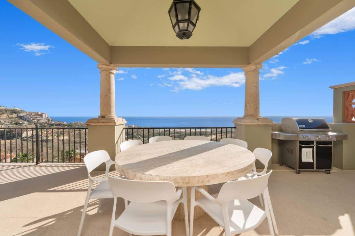 Une terrasse extérieure couverte, avec une table ronde et des chaises, un barbecue et une vue sur la mer.