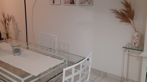 Un comedor con una mesa de vidrio, sillas blancas, una lámpara de pie negra y tres cuadros en la pared.