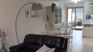 Una sala de estar con un sofá de cuero negro, una mesa de centro de vidrio y un comedor con una mesa y sillas blancas.