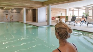 Une piscine intérieure offrant une vue dégagée sur le bord du bassin, un mur en bois avec une pancarte, et un espace détente avec des fauteuils et une personne se relaxant.