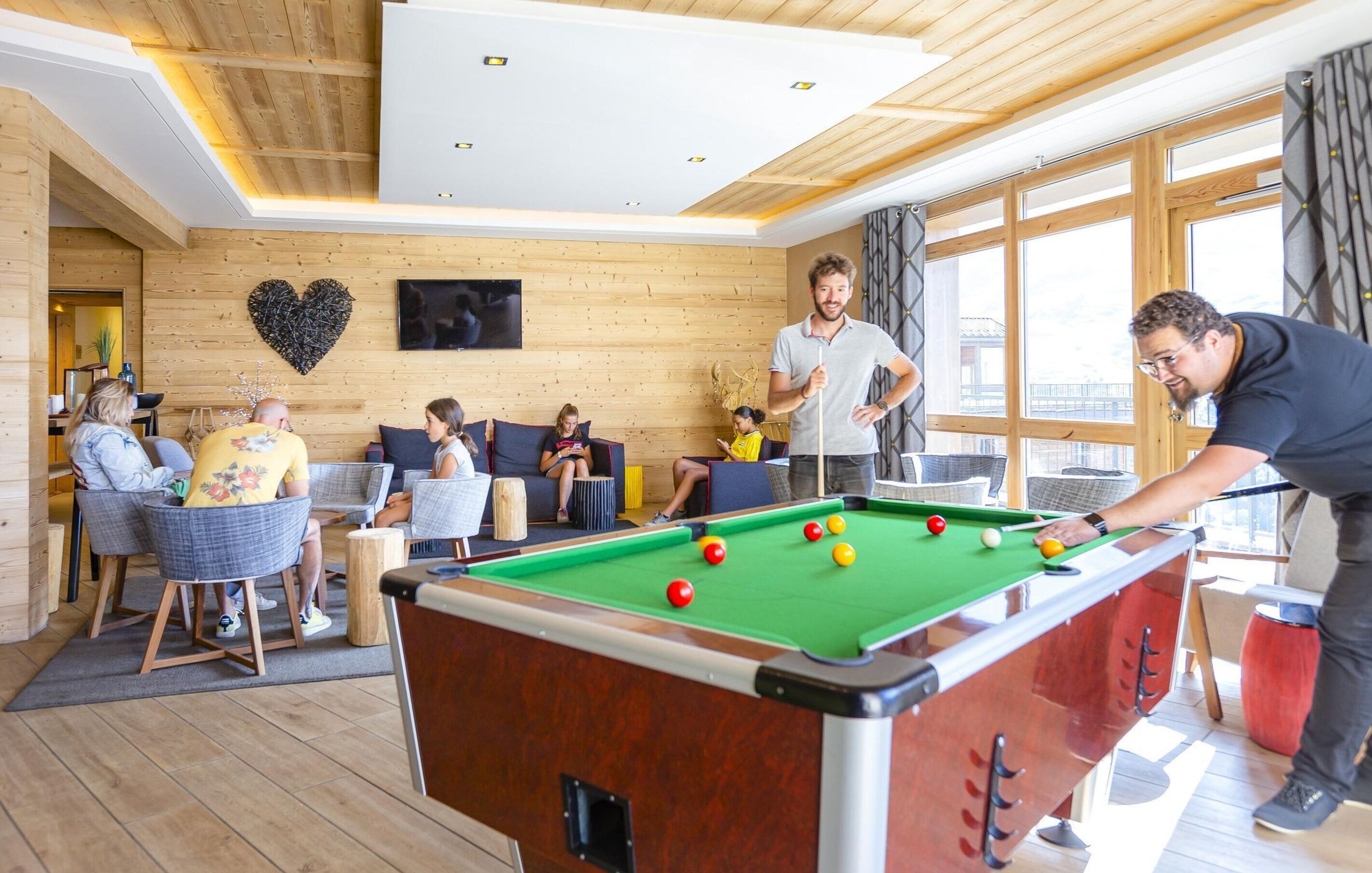 A pool table in a room with wooden walls and large windows.