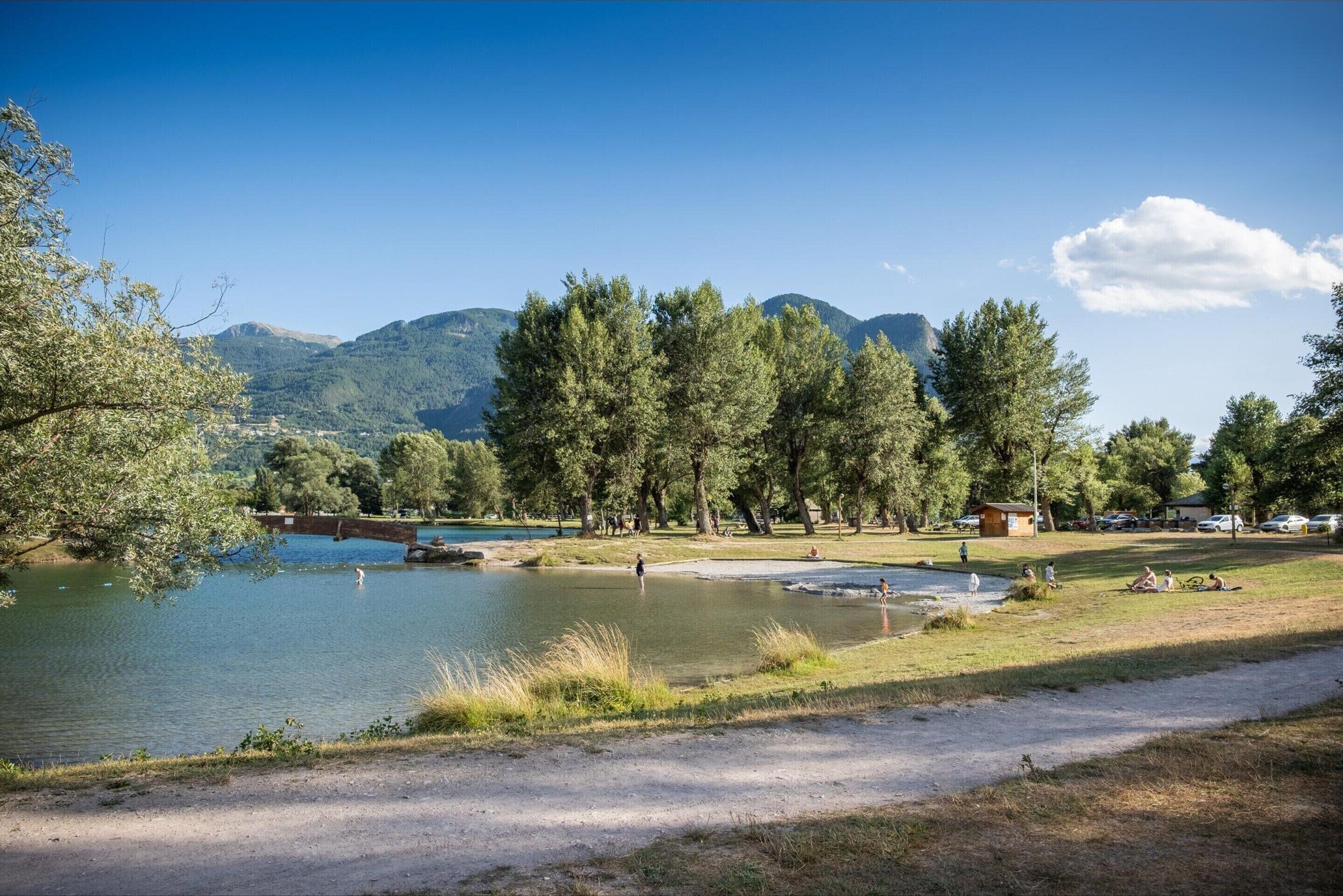 Un parco tranquillo sul lago, con un sentiero sterrato, alberi e un piccolo edificio.