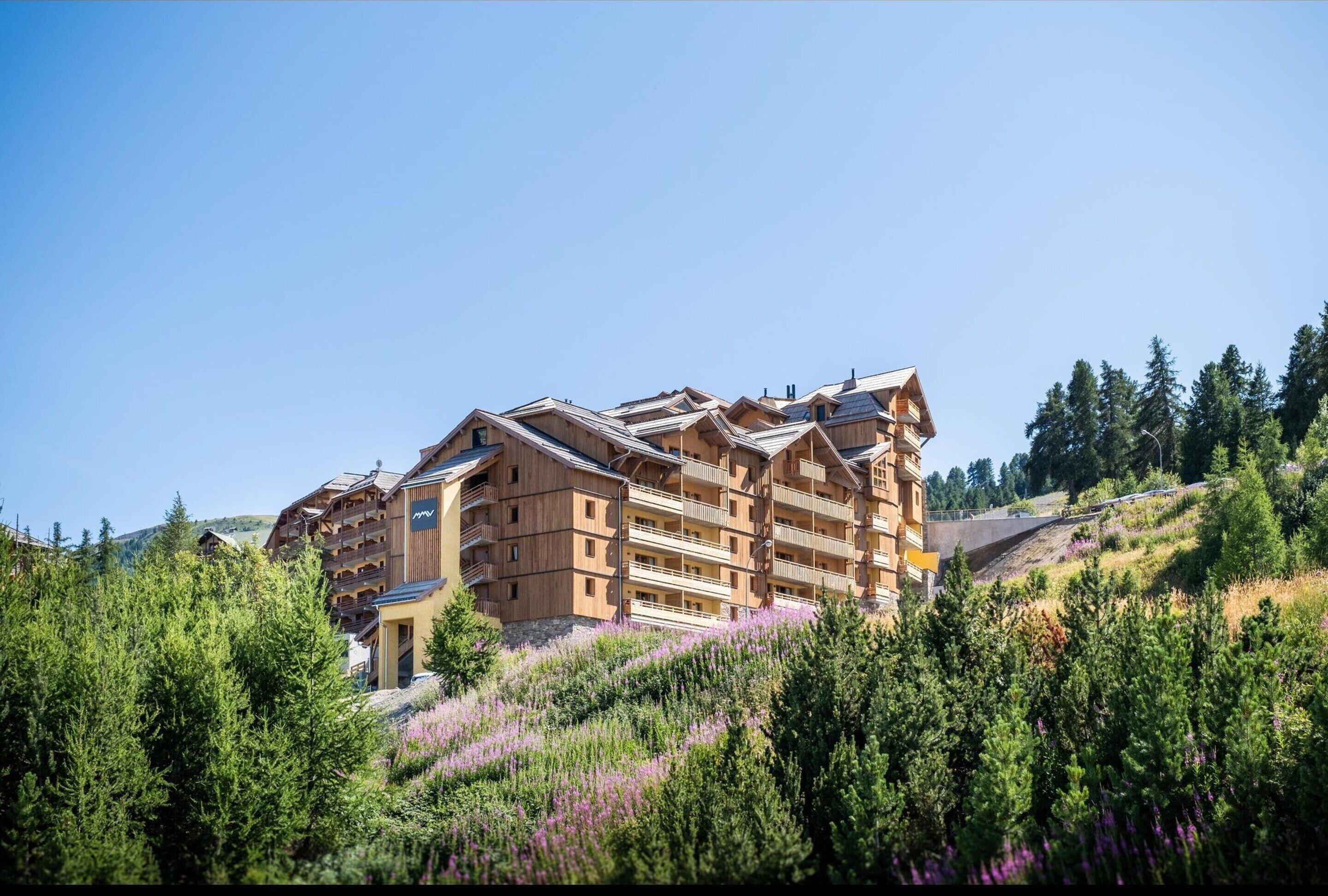Een hotel met meerdere verdiepingen en balkons, omringd door weelderige begroeiing en heuvels.