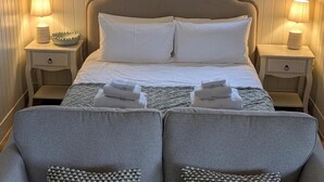 A neatly made bed with white linens, two bedside tables with lamps, and two grey armchairs with patterned cushions. - Not Available for Rent (Whitchurch)