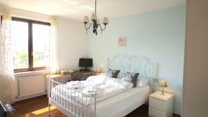 A neatly made bed with white linens, a bedside table with a lamp, and a window with curtains. - Jonah House (Maccagno con Pino e Veddasca)