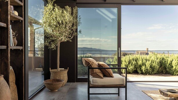 A modern room with a large window, a potted tree, a cushioned chair, and a rustic shelf. - Casa Upupa - Luxury Villa in Tuscany (Toscana)
