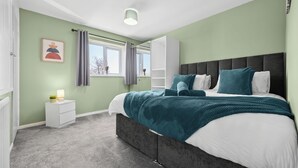 A bedroom with a bed, a nightstand, a window, and a headboard.