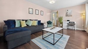 A modern living room with a grey sofa, a white coffee table, and a desk with a laptop.